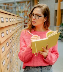 Woman taking notes while looking at card catalog